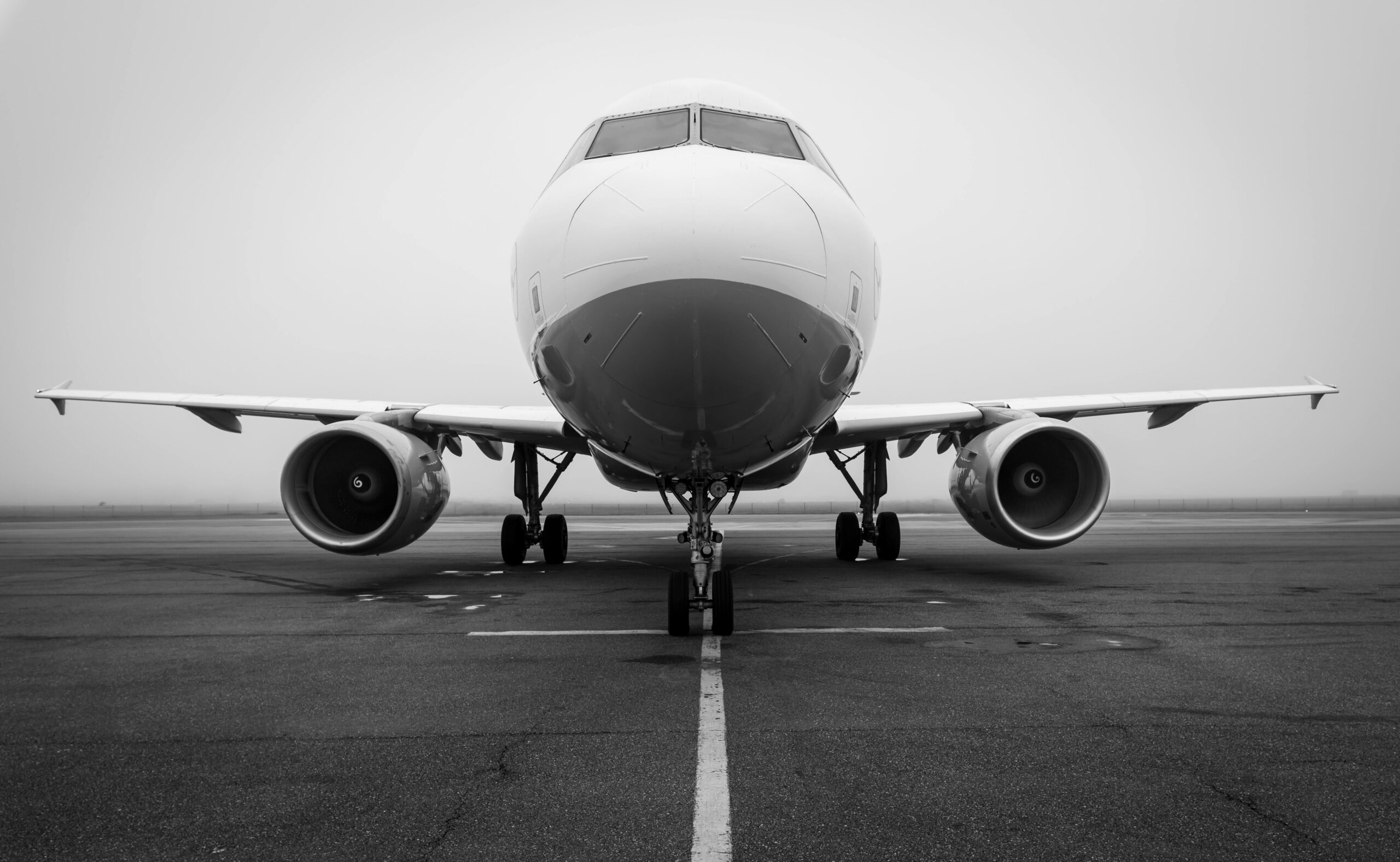 A black and white photo of an airplane on a foggy runway, captured head-on. Ideal for aviation themes.