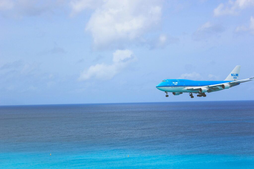 KLM Boeing 747 in flight over a stunning blue ocean with clear skies.